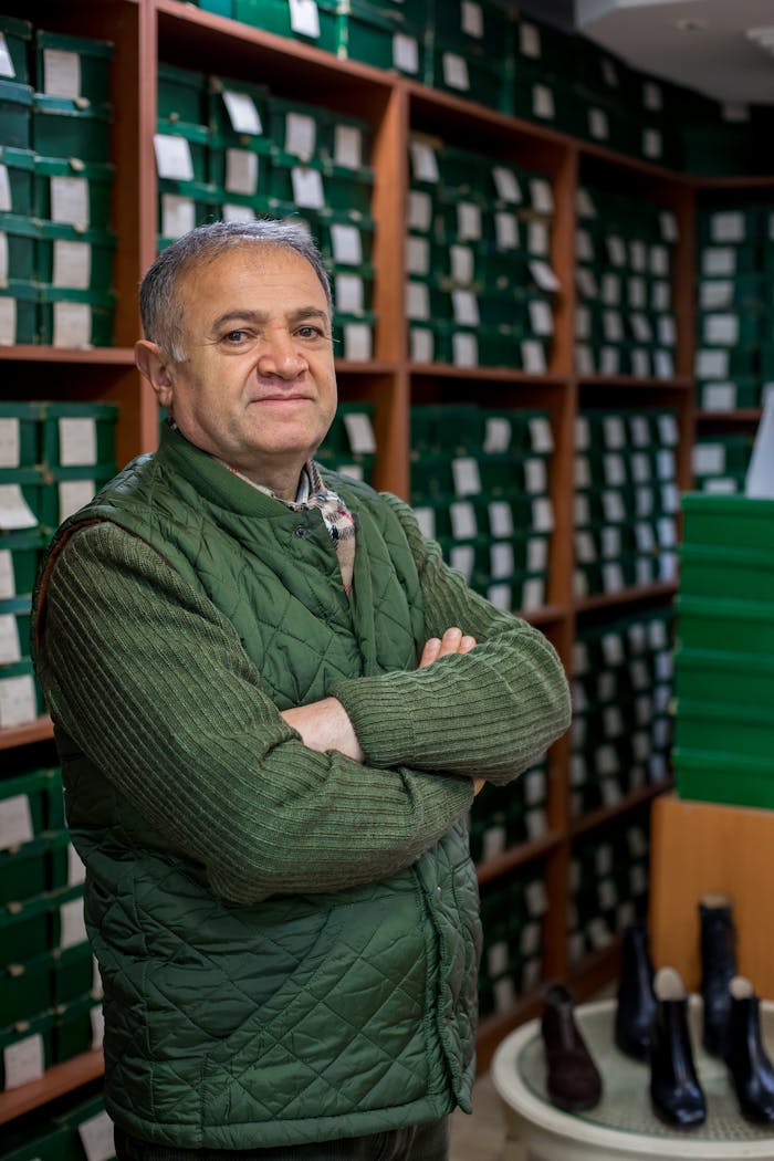 Middle-aged man standing confidently in a shoe store with arms crossed, surrounded by boxes.